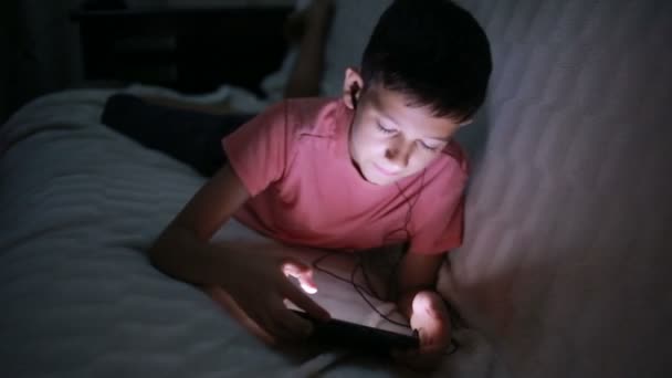 Ung pojke leker med en mobiltelefon eller smartphone på en säng. natt — Stockvideo