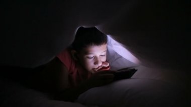 Genç çocuk bir cep telefonu veya bir yatakta smartphone ile oynamak. gece