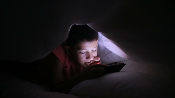 Niño jugando con un teléfono celular o smartphone en una cama. noche — Vídeos de Stock