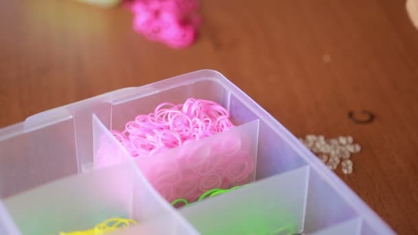 Маленькая девочка плетёт браслеты из резинки. Цветные резиновые ленты для ткачества — стоковое видео