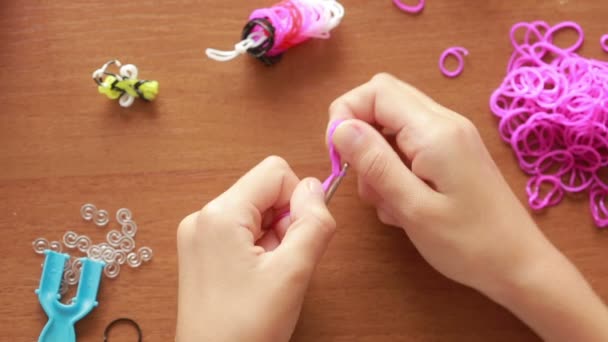 Маленька дівчинка плете браслет з гумок. Кольорові гумки для плетіння — стокове відео