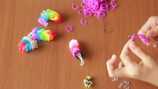 Маленькая девочка плетёт браслеты из резинки. Цветные резиновые ленты для ткачества — стоковое видео
