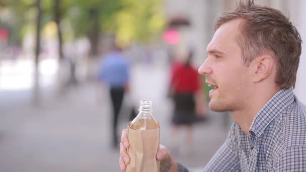 Slordig man drinken van alcohol in de straat. bier in een papieren zak. — Stockvideo