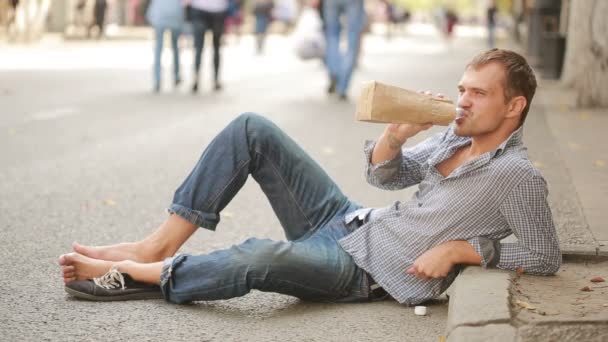 Uomo ubriaco sdraiato sul marciapiede fuori. uomo che beve birra da un sacchetto di carta — Video Stock