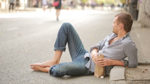 Részeg férfi fekszik a járdán kívül. az ember iszik sört egy papír porzsák — Stock videók