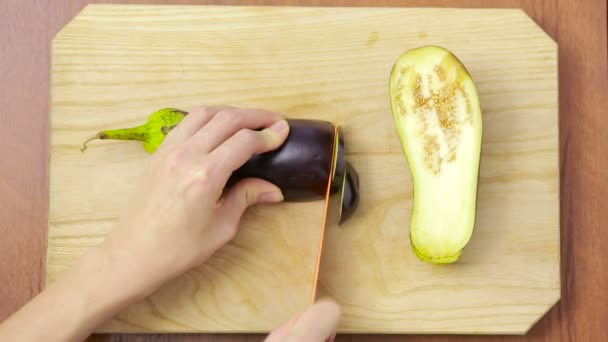 Handen van vrouw snijden aubergine op houten bord. Bekijk van bovenaf. bovenaanzicht — Stockvideo