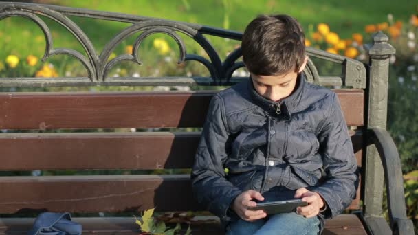 Boy venku na podzim sedí na lavičce v bundě a využití smartphone — Stock video