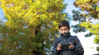 Çocuk açık havada bir ceket ve kullanımı bir smartphone bankta oturmuş Güz