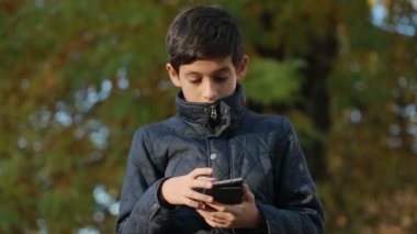 Çocuk açık havada bir ceket ve kullanımı bir smartphone bankta oturmuş Güz