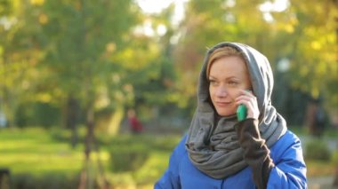 Sonbahar parkta cep telefonuyla konuşan genç gülümseyen kadın.