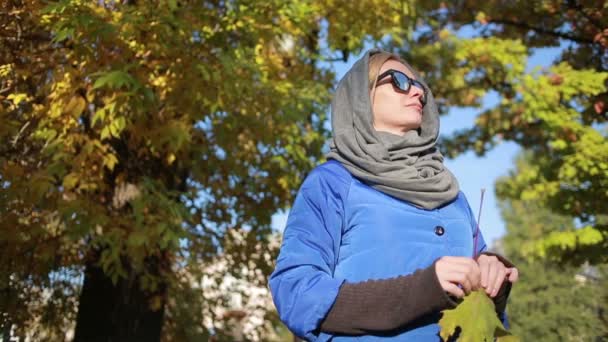 Mooie vrouw in zonnebril in herfst park. Houdt de handen gele bladeren — Stockvideo