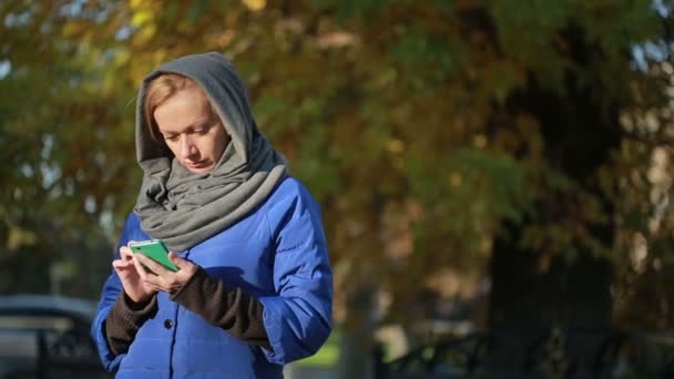 Mladá usměvavá žena mluví do mobilního telefonu v podzimní park. — Stock video