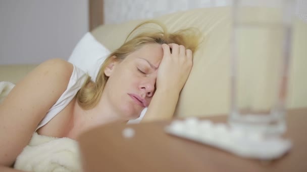 Zieke vrouw liggend op het bed. pillen en glas water. Drink tabletten. pijnstiller — Stockvideo