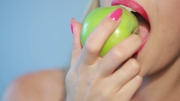 Mooi meisje eet een groene appel op een blauwe. Close-up — Stockvideo