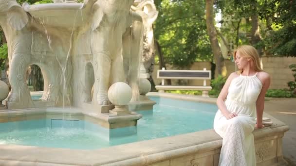 Schönes junges Mädchen im Kleid, das in der Nähe des Steinbrunnens steht. — Stockvideo