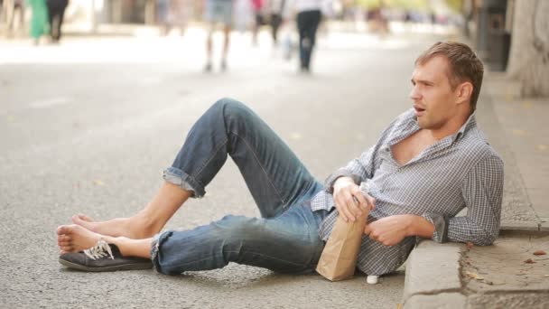 Homem bêbado deitado no pavimento lá fora. homem bebendo cerveja de um saco de papel — Vídeo de Stock