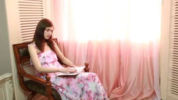 Mujer en casa sentada en silla delante de la ventana libro de lectura — Vídeos de Stock