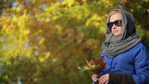 Vacker kvinna i solglasögon i höst park. Håller händerna gula blad — Stockvideo