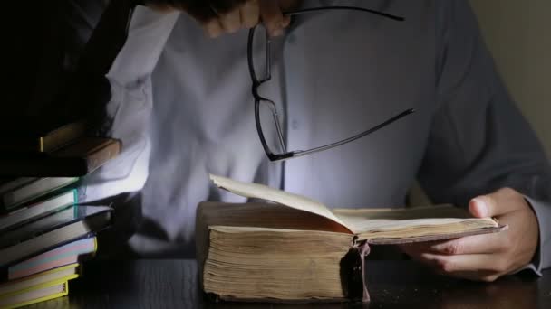 Homem inteligente estudando tarde da noite, ele está sentado na mesa e lendo livro — Vídeo de Stock