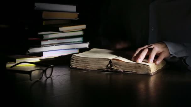 Homem inteligente estudando tarde da noite, ele está sentado na mesa e lendo livro — Vídeo de Stock