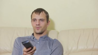 Uzaktan kumandalı bir adam evde televizyon izliyor.