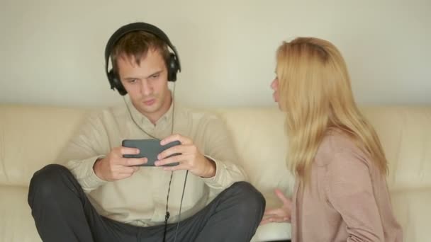 Woman yells at man with headphones. Husband plays on the smartphone — Stock Video