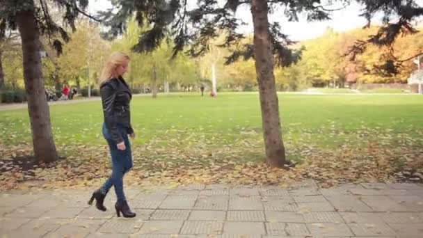 Красивая молодая женщина в осеннем парке. блондинка в кожаной куртке — стоковое видео
