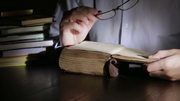 Un hombre inteligente que estudia hasta tarde en la noche, está sentado en el escritorio y leyendo un libro — Vídeo de stock