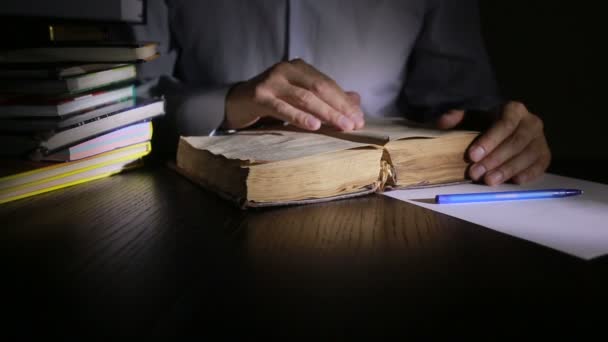 Homem inteligente estudando tarde da noite, ele está sentado na mesa e lendo livro — Vídeo de Stock