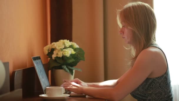 Beautiful woman working on a laptop sitting on the table in the house. — Stock Video