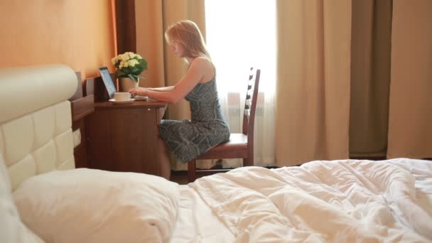 Schöne Frau arbeitet an einem Laptop, der auf dem Tisch im Haus sitzt. — Stockvideo