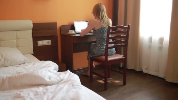 Beautiful woman working on a laptop sitting on the table in the house. — Stock Video