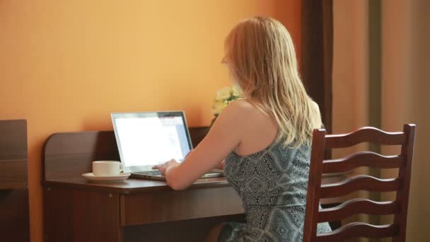 Mooie vrouw bezig met een laptop die zittend op de tafel in het huis. — Stockvideo