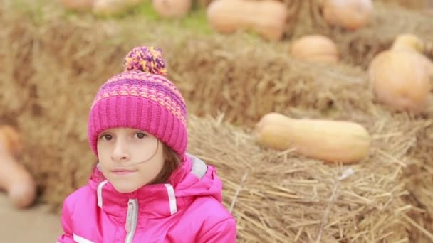 Маленька дівчинка сидить на сіні, прикрашена гарбузами, чекає відпустки — стокове відео