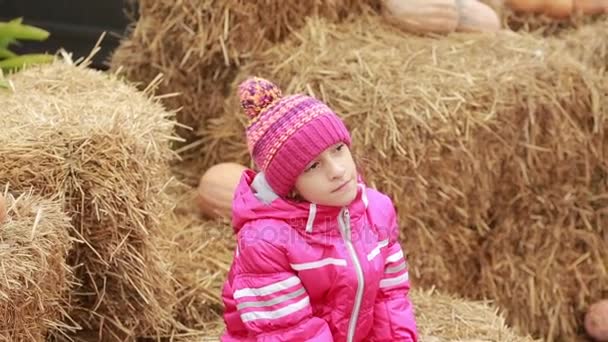 Little girl sitting on the hay, decorated pumpkins, waiting for holiday — Stock Video