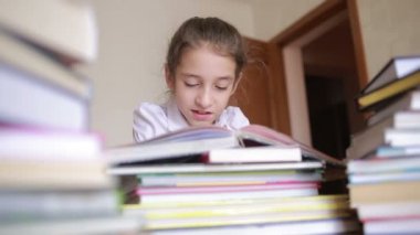 Okulun tek tip küçük kızı kitap yığınları arasında oturup kitap okumak