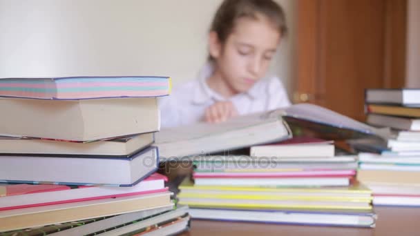 Niña en uniforme escolar está leyendo un libro, sentado entre montones de libros — Vídeos de Stock