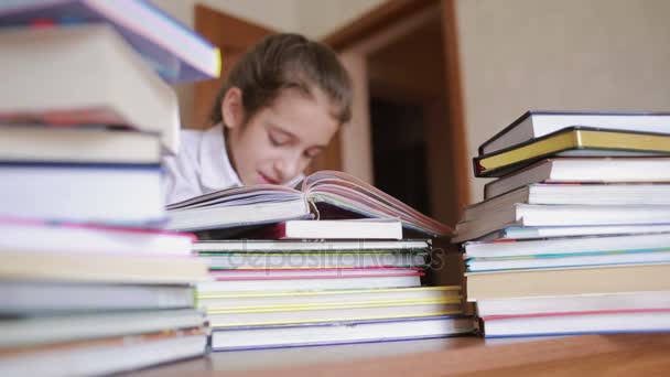 Petite fille en uniforme scolaire lit un livre, assis entre des piles de livres — Video