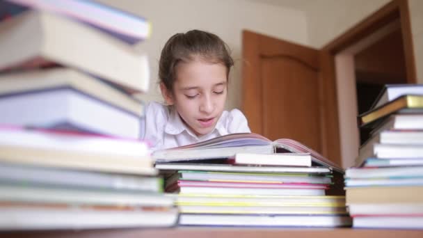 Petite fille en uniforme scolaire lit un livre, assis entre des piles de livres — Video