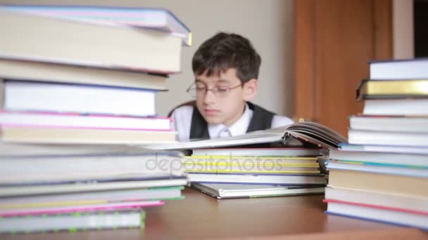 Pojke sitter vid ett bord med en trave böcker. barn läsa. pojke med glasögon — Stockvideo