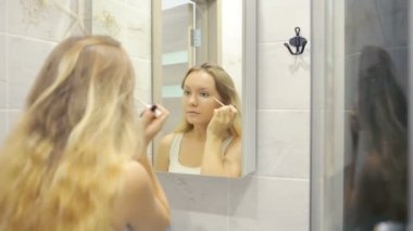 Güzel genç kadın aynanın önünde makyaj yapıyor.