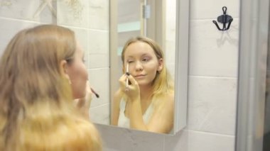 Güzel genç kadın aynanın önünde makyaj yapıyor.