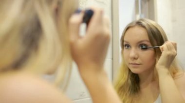 Güzel genç kadın aynanın önünde makyaj yapıyor.