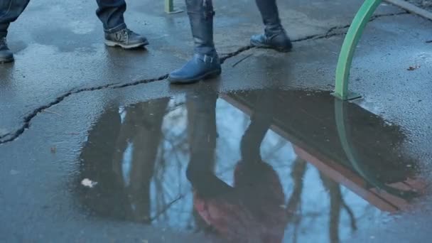 Дівчина в чорних бойових черевиках бризкає в калюжі після дощу — стокове відео