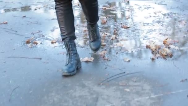 Девушка в черных боевых сапогах брызгает в лужу после дождя — стоковое видео