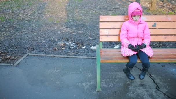 Niña bonita sentada en un banco y triste en el parque en otoño — Vídeos de Stock