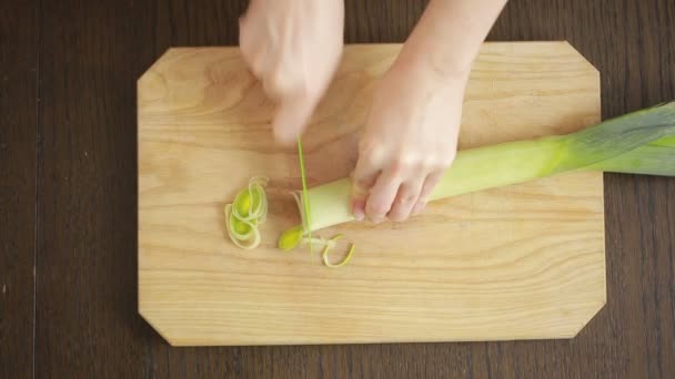 Zenske ruku s nožem řezy pórku na dřevěné desce v kuchyni. — Stock video