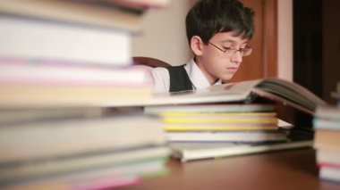 kitapların bir yığınına bir masada oturan çocuk. Çocuk okuma. gözlüklü çocuk