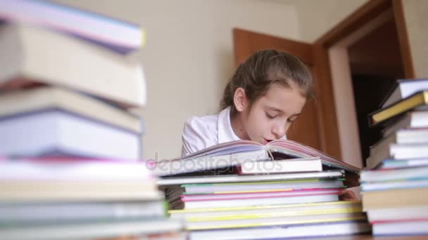 Маленькая девочка в школьной форме читает книгу, сидит между стопками книг — стоковое видео