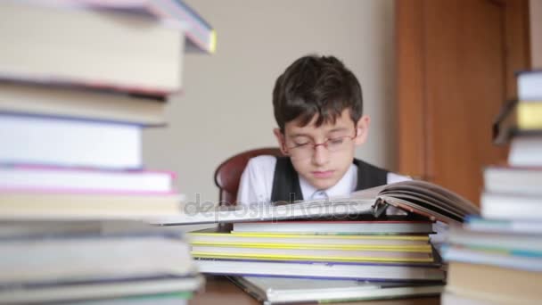 Rapaz sentado numa mesa com uma pilha de livros. leitura de crianças. menino com óculos — Vídeo de Stock